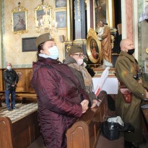 Dwie kobiety oraz mężczyzna ubrani w stroje wojskowe stojąc przy ławkach uczestniczą we mszy w kościele.